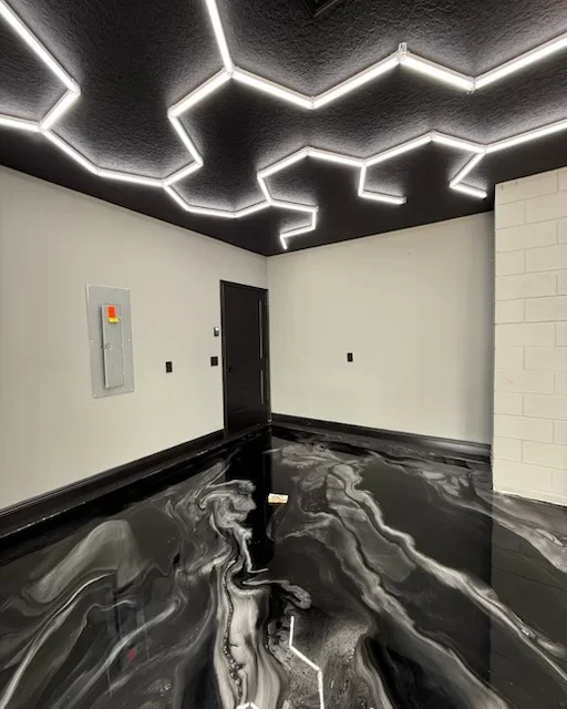 Black and white marbled epoxy floor with geometric neon ceiling lighting and white subway tile walls