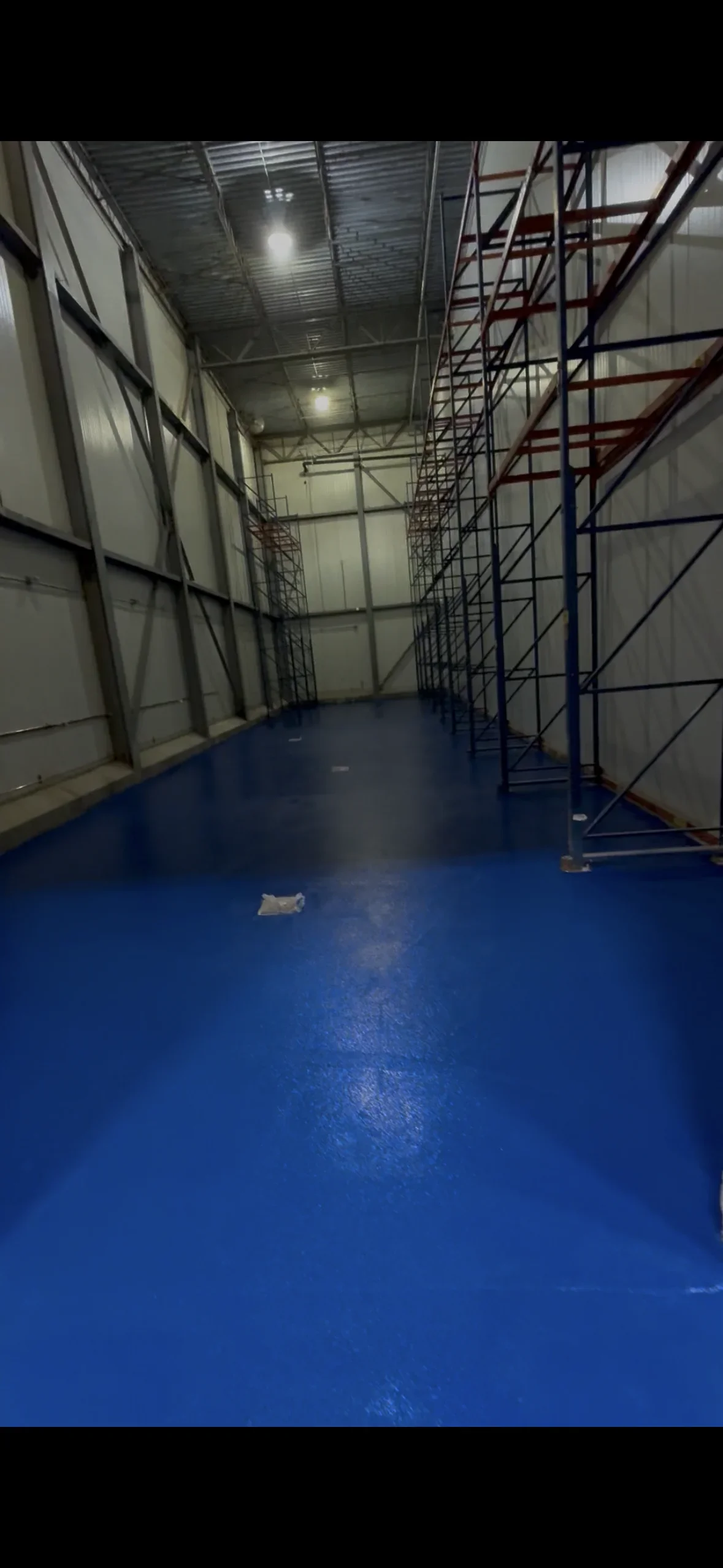 Blue epoxy floor coating in industrial warehouse with metal scaffolding and corrugated metal walls