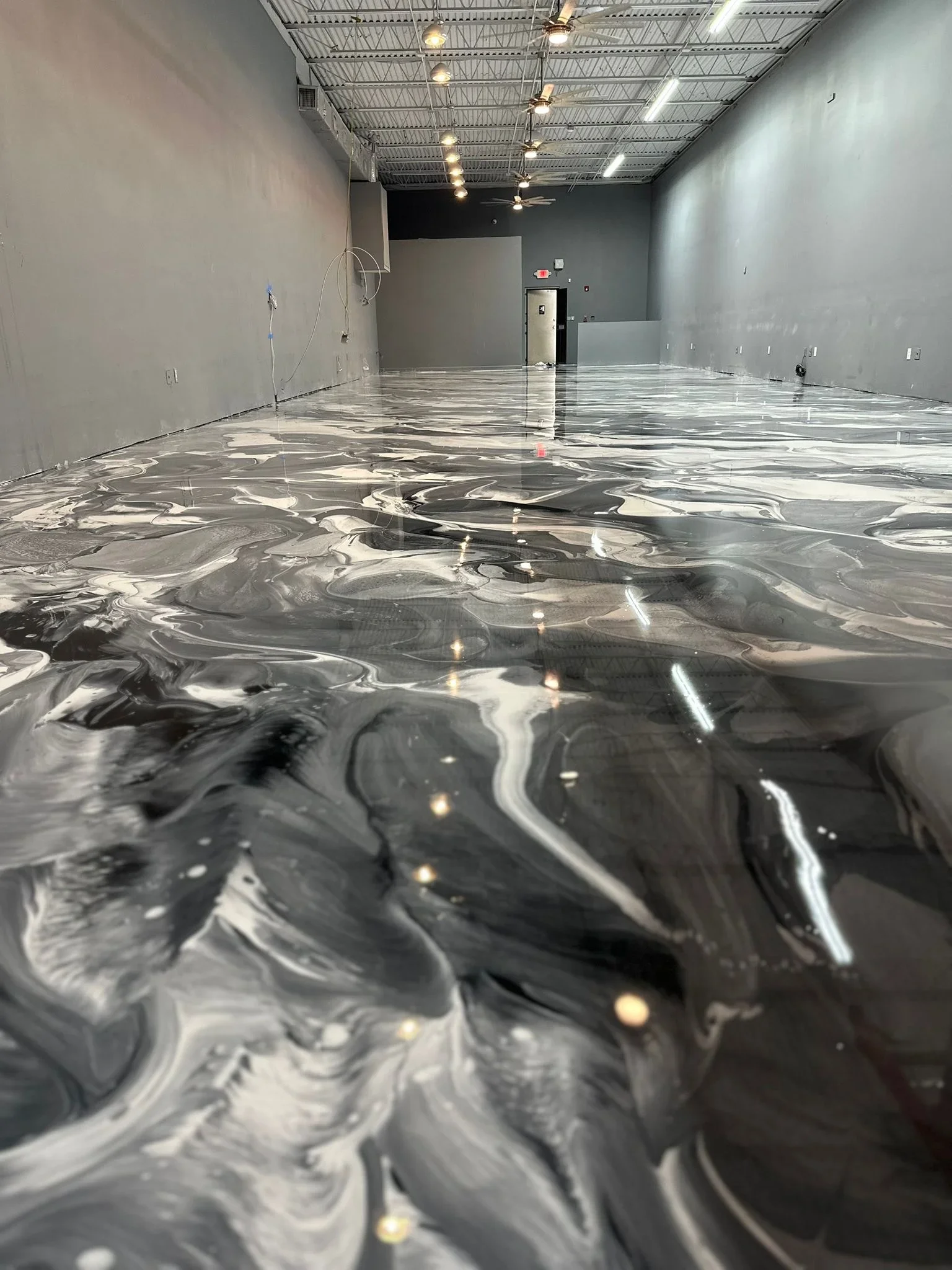Metallic epoxy floor with black and white swirl pattern in commercial warehouse space
