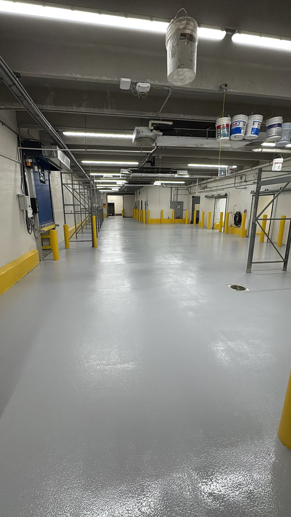 Industrial warehouse with gray epoxy floor coating, yellow safety bollards, and LED lighting