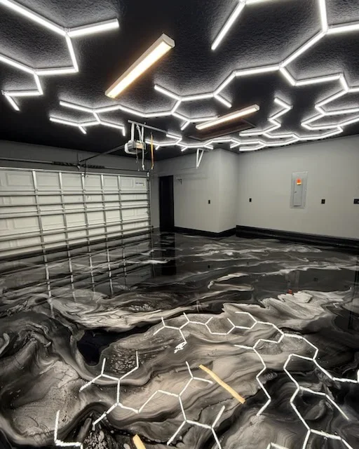 Metallic epoxy garage floor with black and gray swirls, white neon geometric ceiling design, and LED lighting