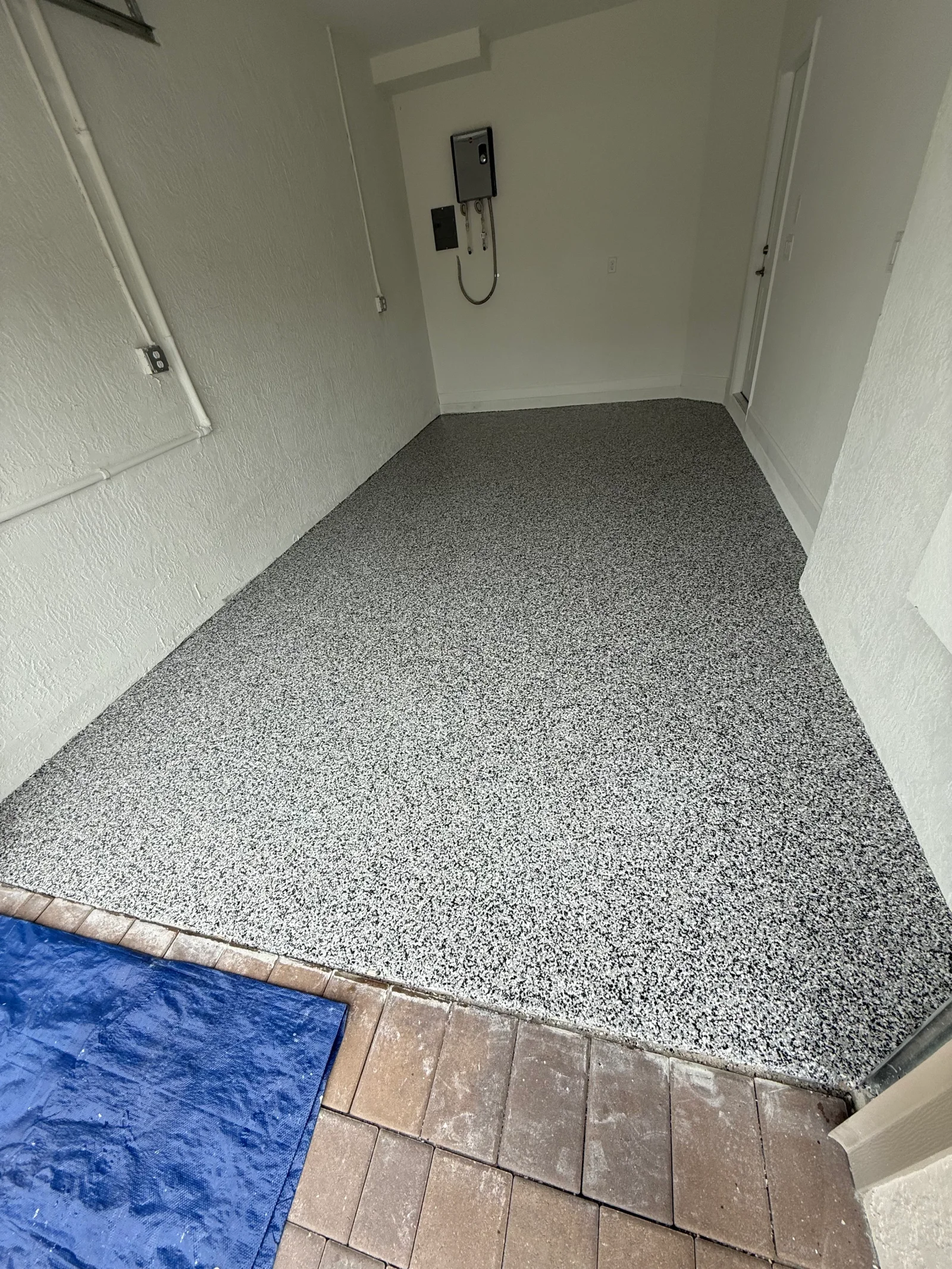 Gray speckled epoxy floor coating in garage with white walls and electrical outlet