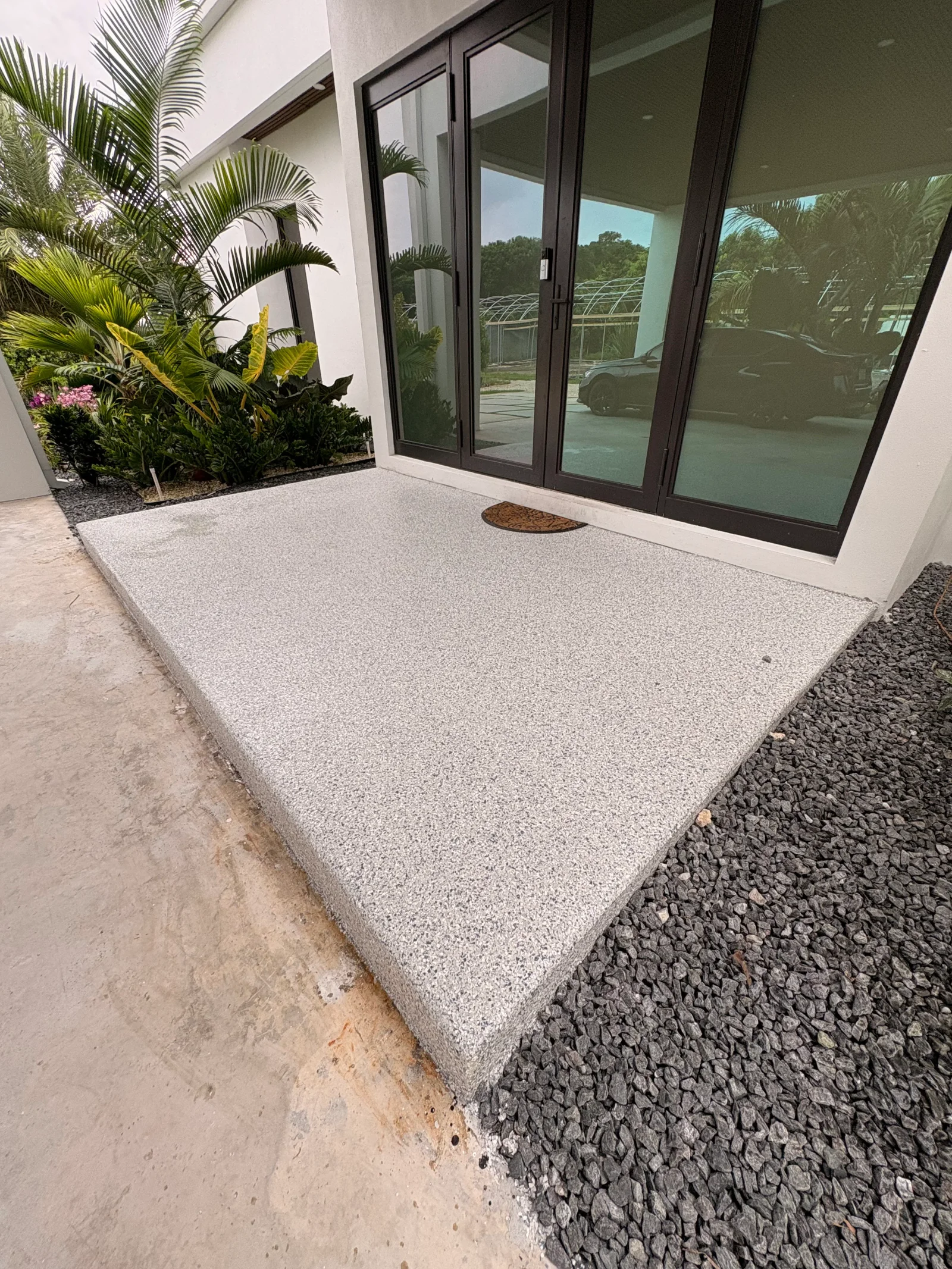 Light aggregate resin patio with black-framed glass doors and tropical landscaping