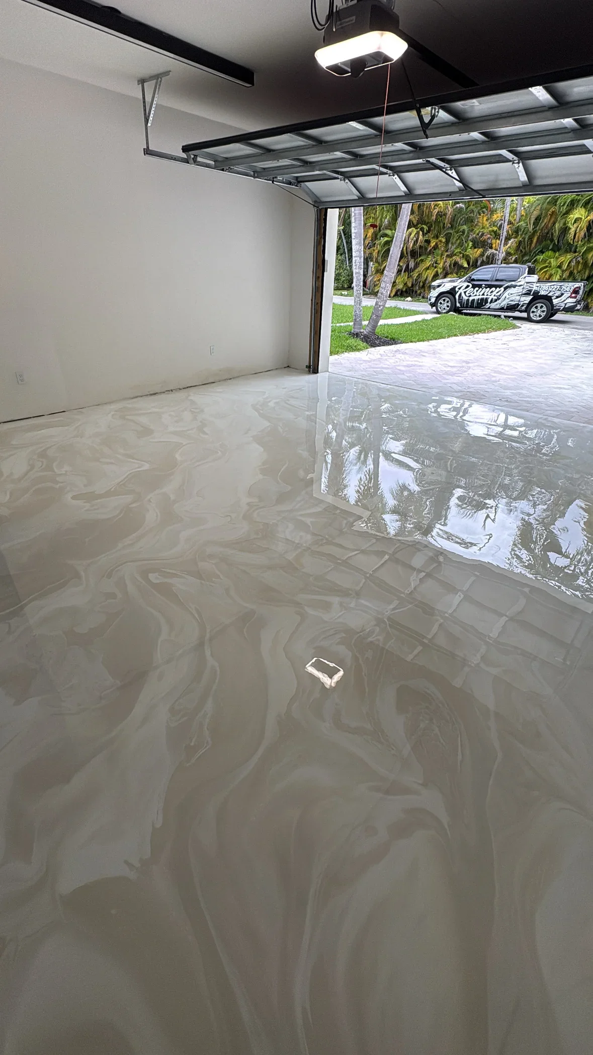 Glossy epoxy garage floor with swirl pattern, open garage door, and driveway visible